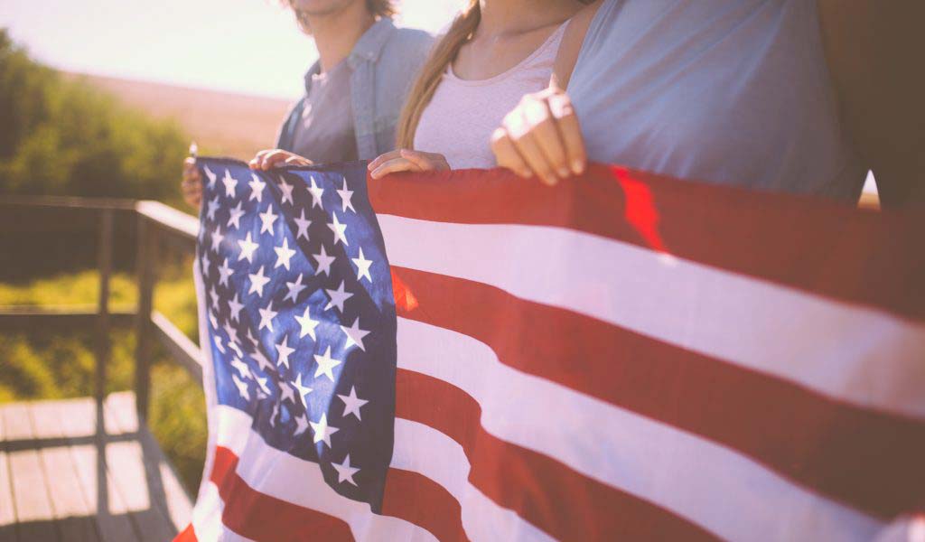 Cropped shot of a row of three youth holding an American flag with a vintage style develop outdoors