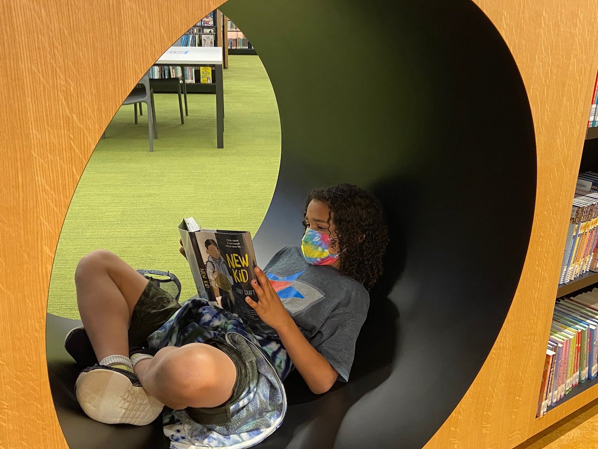 A military child sits in a circular reading nook, reading a book, in the Martin Luther King library.