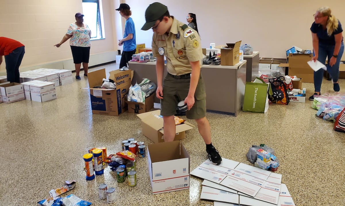 Boy Scout, Gavyn, works alongside volunteers packing boxes with collected donations.