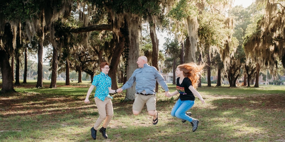 A family holding hands and jumping with smiles on their faces.