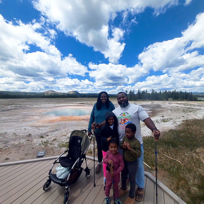 family posing in front of springs at Yellowstone National Park