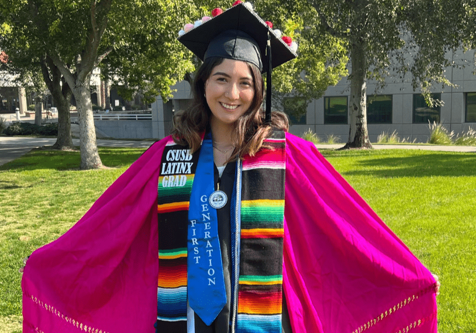 DEPLOY Fellow Andrea poses in a colorful graduation gown and sashes.