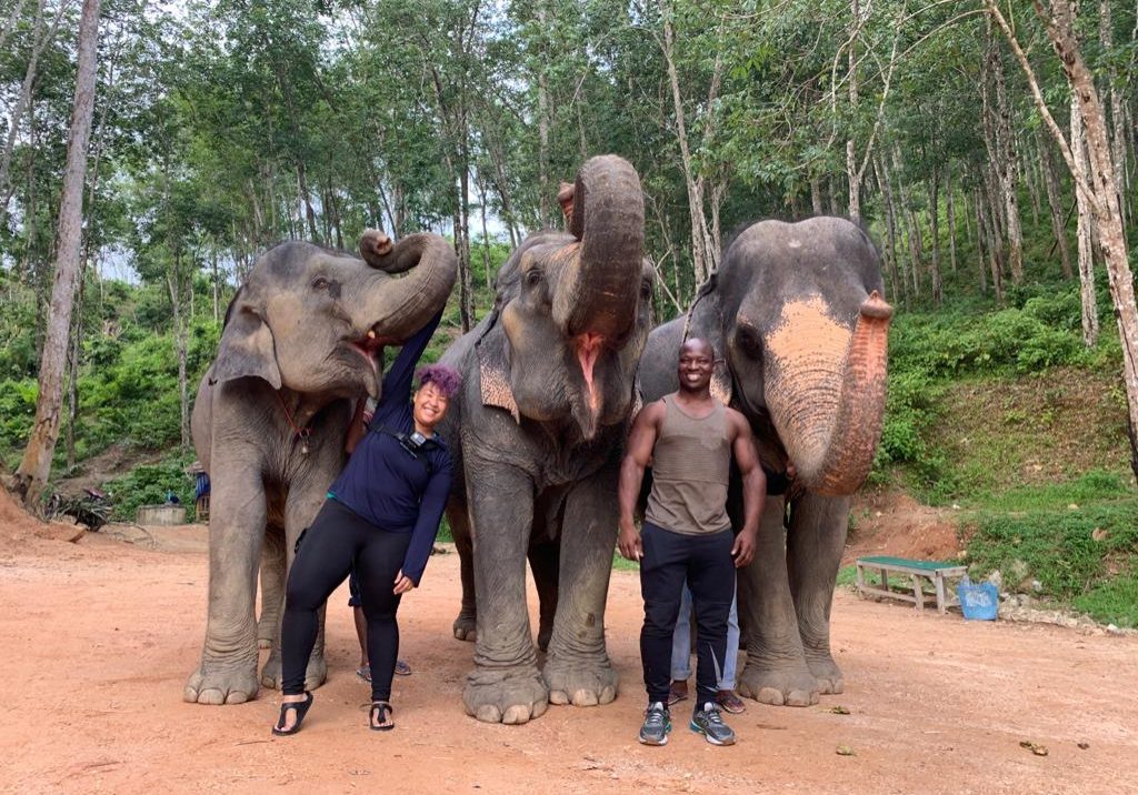 Kimberly poses in front of three large elephants with her husband.