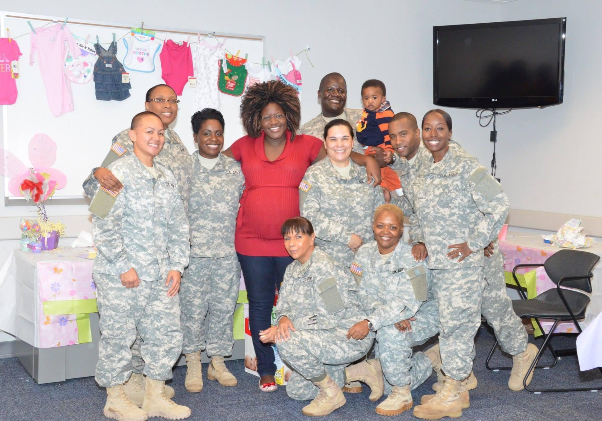 An expecting Lydiah poses in the middle, standing alongside her husband, son, and eight other soldiers at her baby shower.